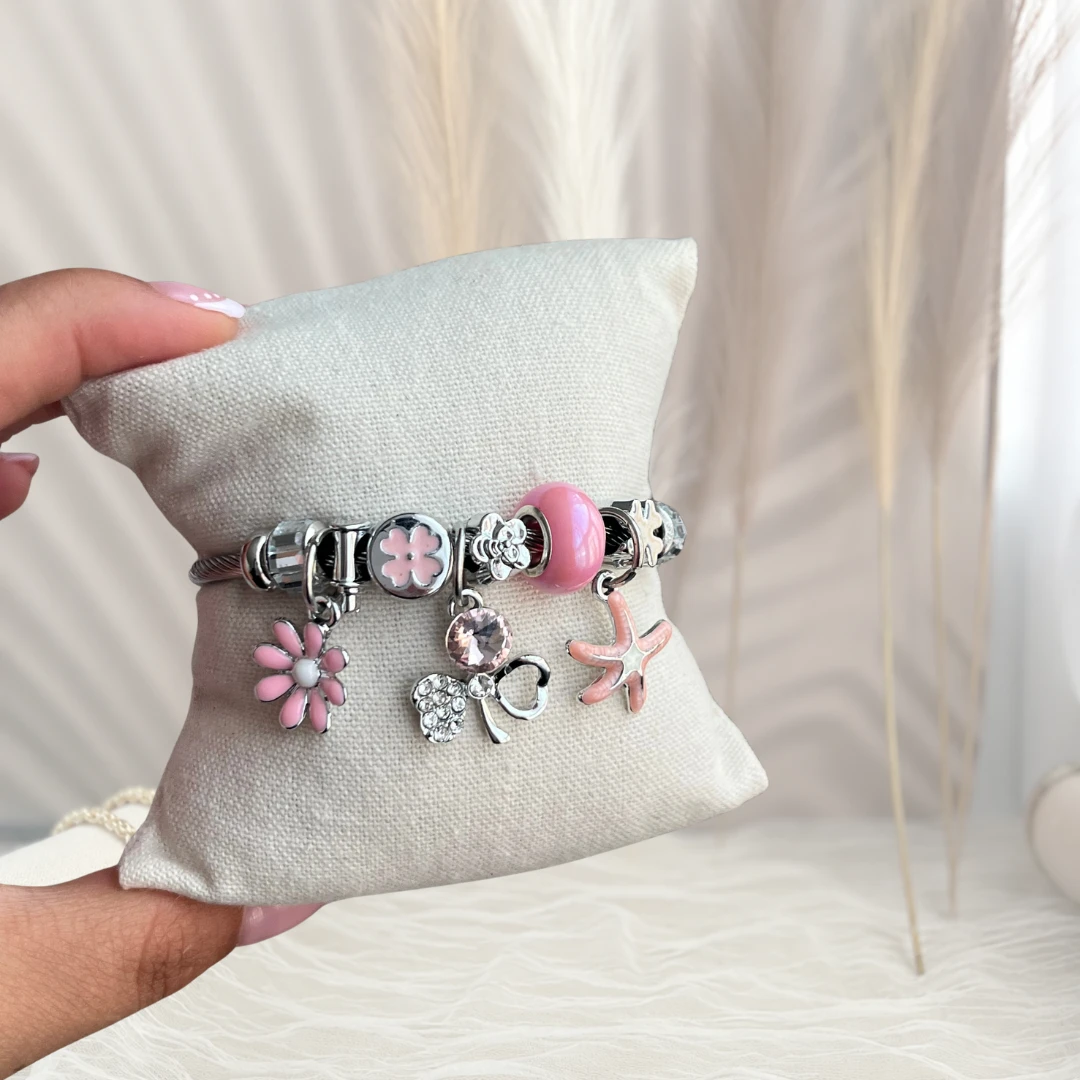Pulsera de charms en rodio con dijes rosados sobre un cojín de exhibición